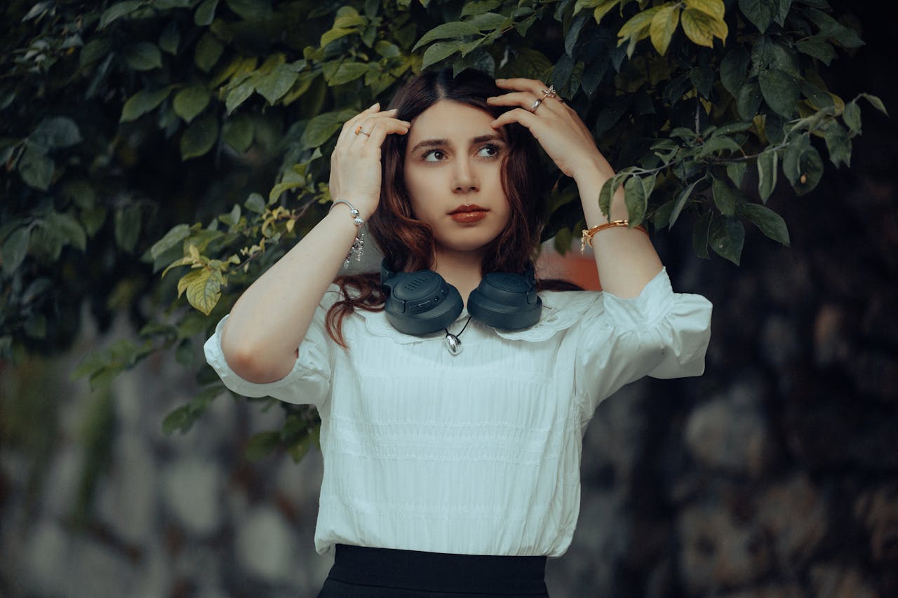 Young woman with headphones poses outdoors in natural leafy setting.