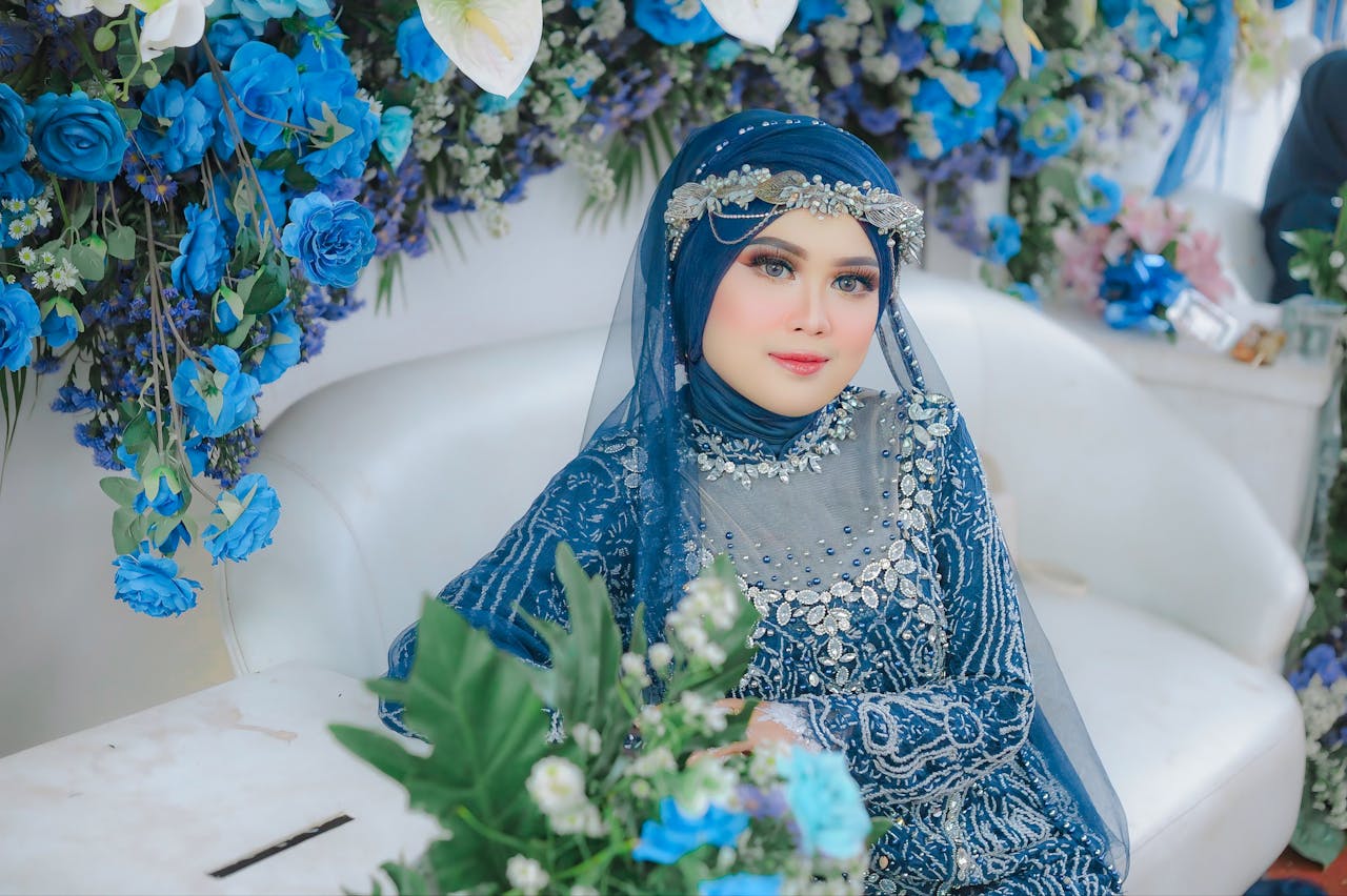 who-we-are Stunning portrait of a woman in ornate blue attire amid lush floral decorations.